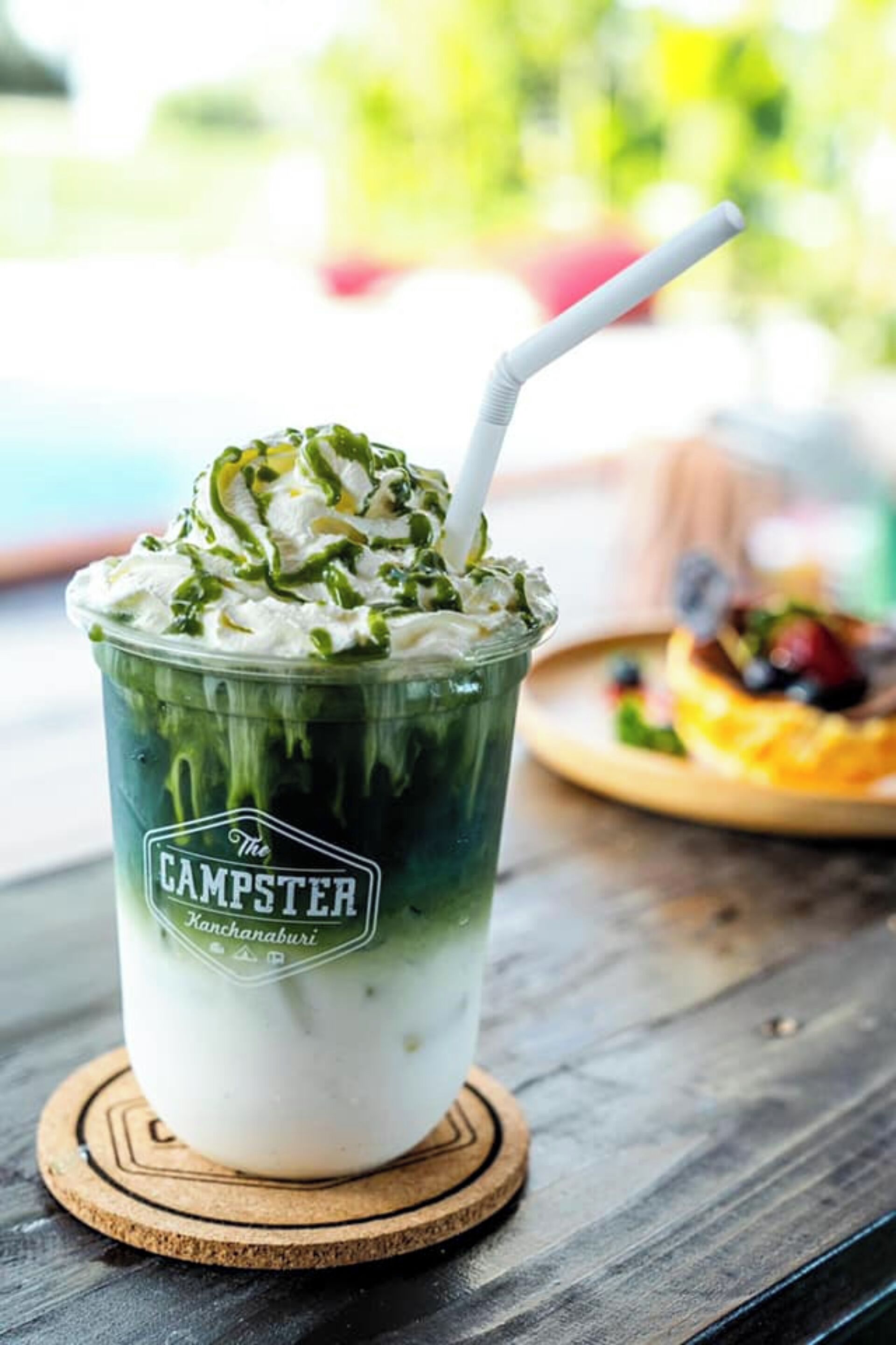 A layered beverage in a branded cup with a straw, placed on a wooden coaster.