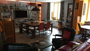 Un salon confortable avec un canapé en cuir, une table à manger avec des chaises et un coin cuisine doté d’étagères et d’un téléviseur.