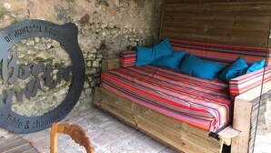 Un lit en bois rustique, agrémenté de draps rayés aux couleurs vives et de coussins bleus, un mur en pierre et une chaise en bois.