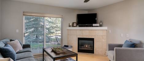 A modern living room with a fireplace, a flat-screen TV, and a ceiling fan.