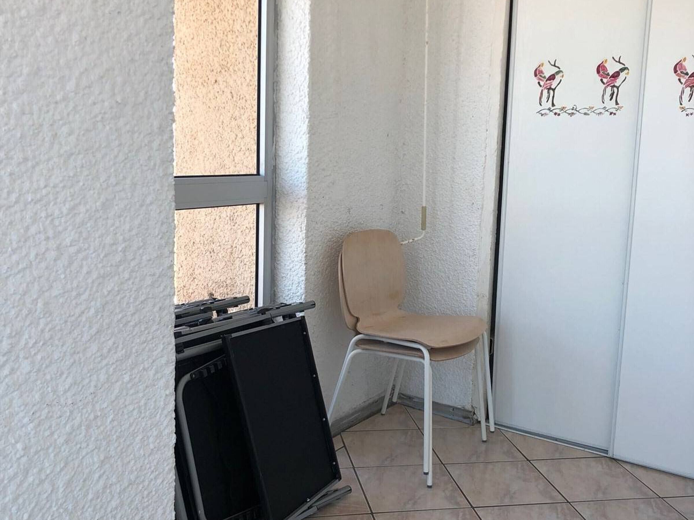Une pièce d’angle avec une fenêtre, une chaise et une porte ornée d’un motif représentant un oiseau.