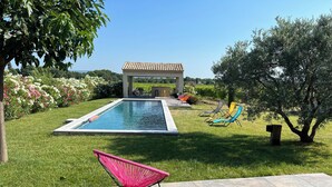 A swimming pool with a pergola, a grassy area, and lounge chairs.