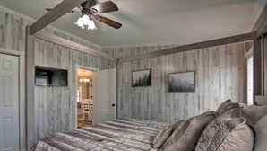 A bedroom with a large bed, a ceiling fan, and a TV mounted on the wall.
