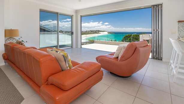 Una sala de estar moderna con un amplio ventanal que da a un balcón con vista a una playa y el océano.