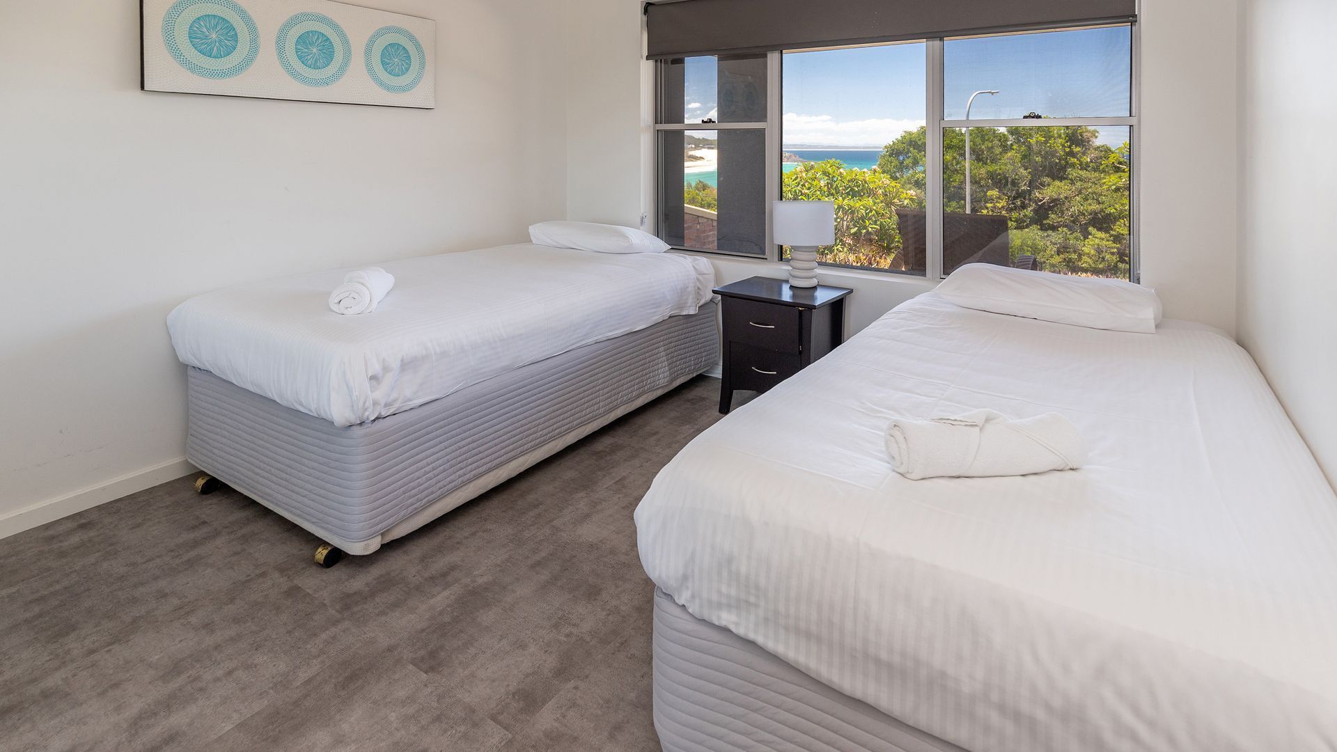 Quarto com duas camas, uma mesinha de cabeceira e janela vista para o mar.