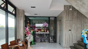 A modern interior with a reception desk, wooden chairs, and a stone wall. - Samutsakorn Apartment (Samut Sakhon)