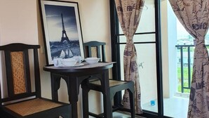 A room with a bed, a table with a framed picture of the Eiffel Tower, two chairs, and a balcony with curtains. - Samutsakorn Apartment (Samut Sakhon)