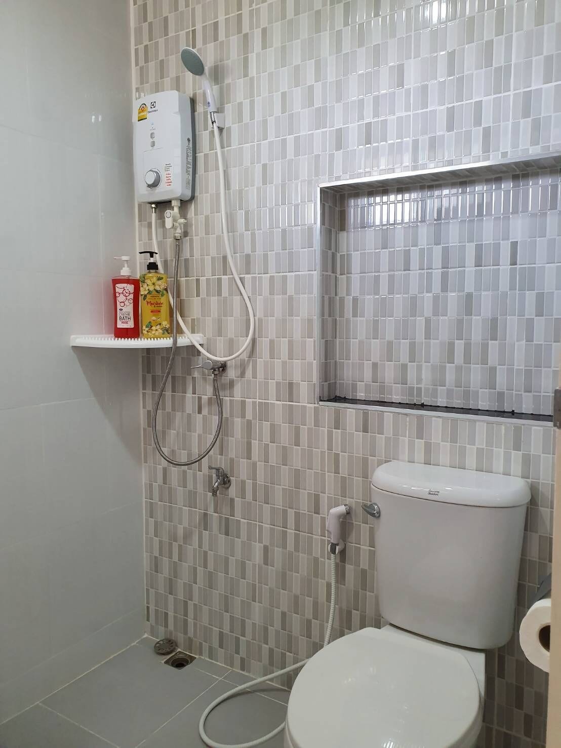 Un baño con inodoro, ducha y pared con azulejos.