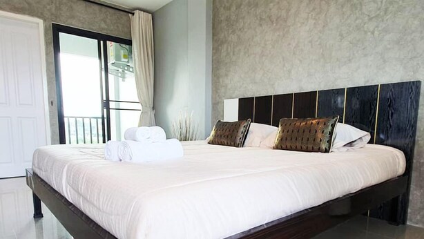 A large bed with white linens, a dark headboard, and two decorative pillows. - Samutsakorn Apartment (Samut Sakhon)