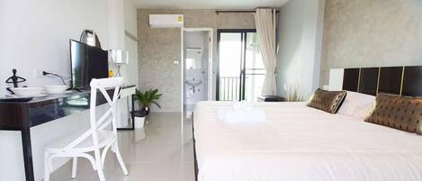 A modern hotel room with a large bed, a desk with a computer, and a bathroom visible through an open door.