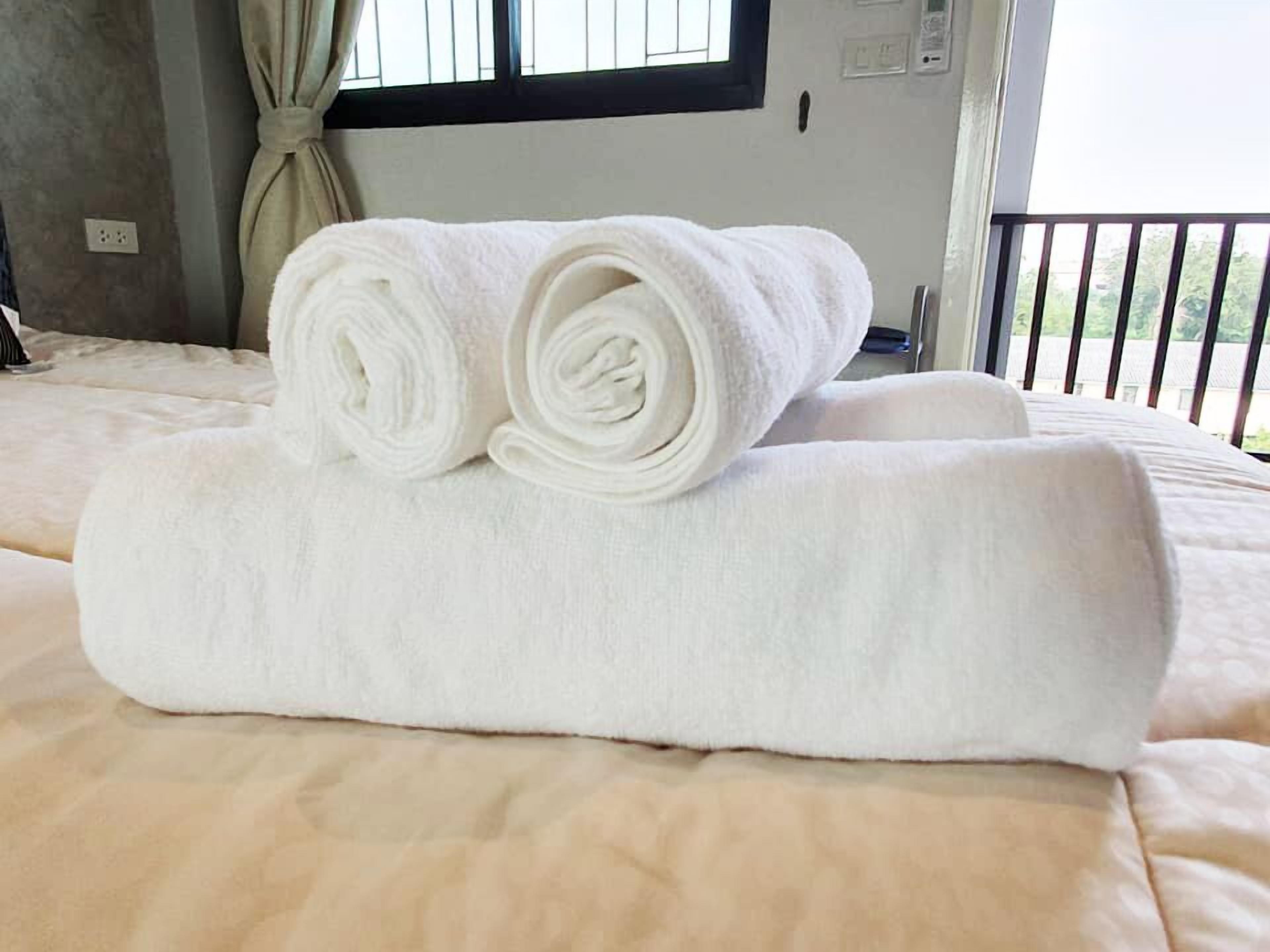 A neatly made bed with a rolled white towel on top.