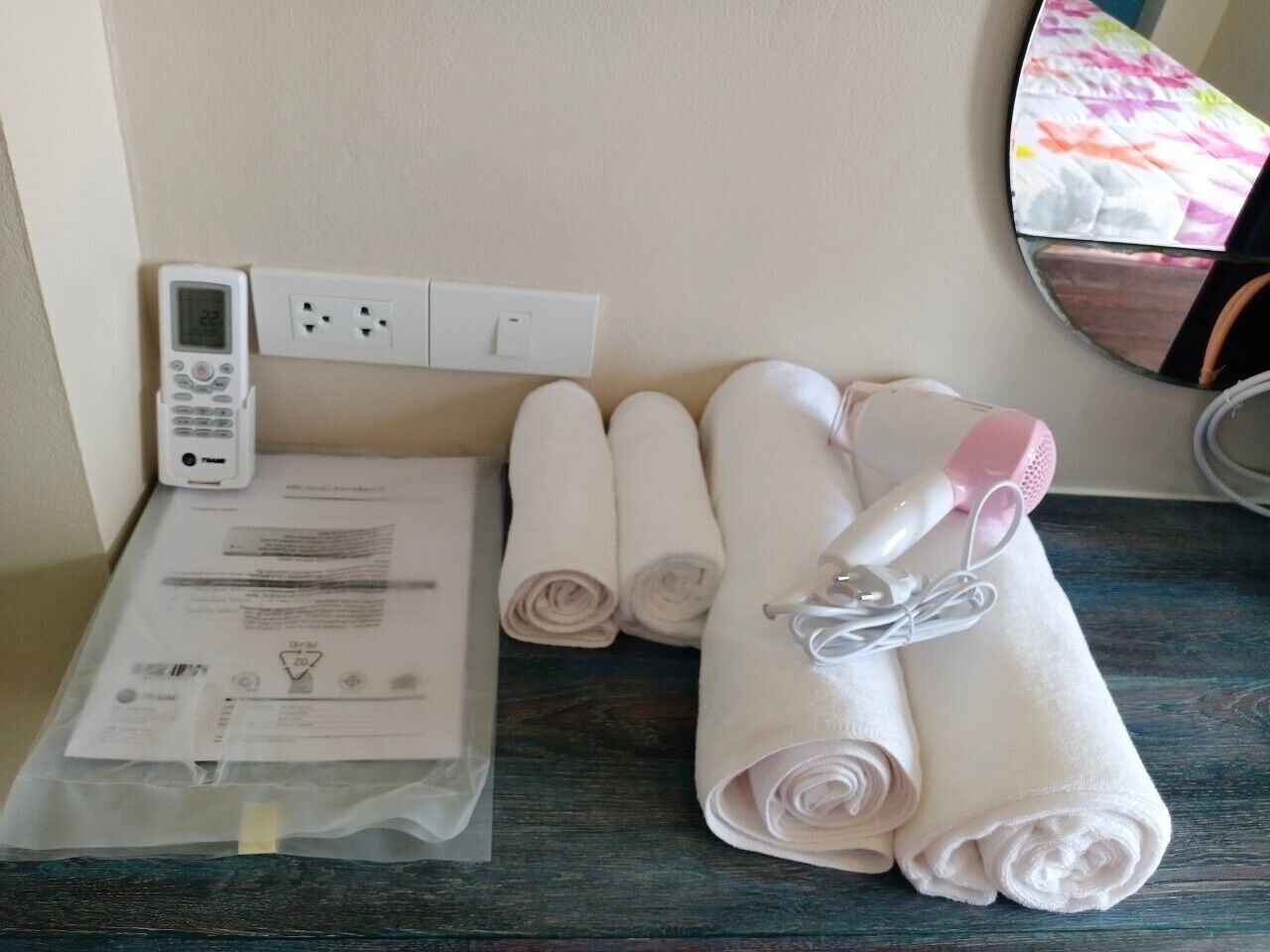 A bathroom with a towel rack holding rolled towels, a hairdryer, and a digital thermostat on the wall.