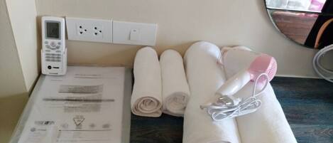 A bathroom with a towel rack holding rolled towels, a hairdryer, and a digital thermostat on the wall.