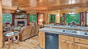 Een knus chaletinterieur met een open haard, houten plafond, een eetgedeelte en een keuken met vaatwasser.