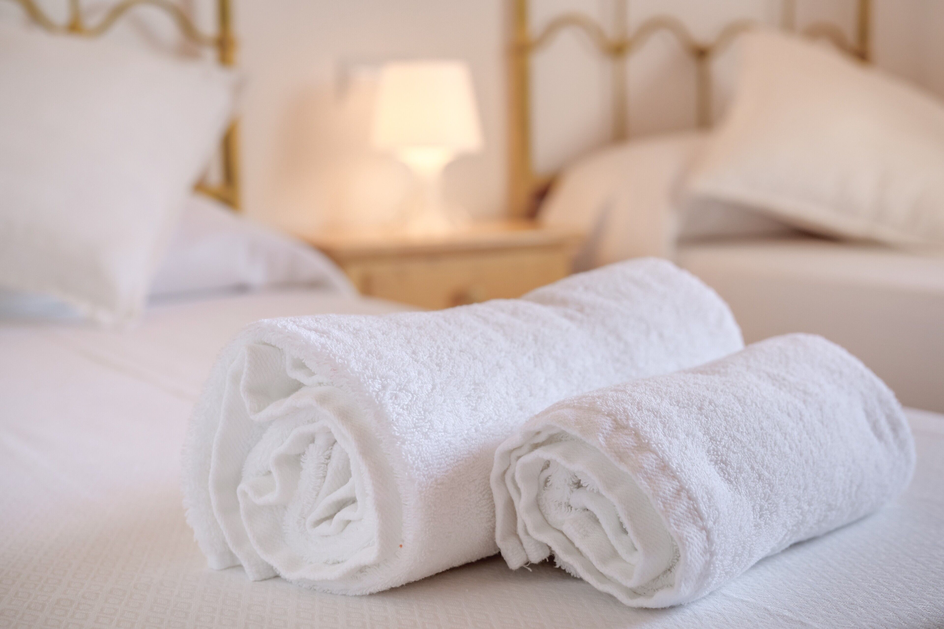 Un lit bien fait, avec des draps blancs et une serviette blanche enroulée posée sur le dessus.