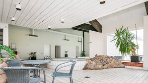 Uma área interna de piscina moderna com paredes de pedra, um espaço de estar com cadeiras e plantas em vasos.