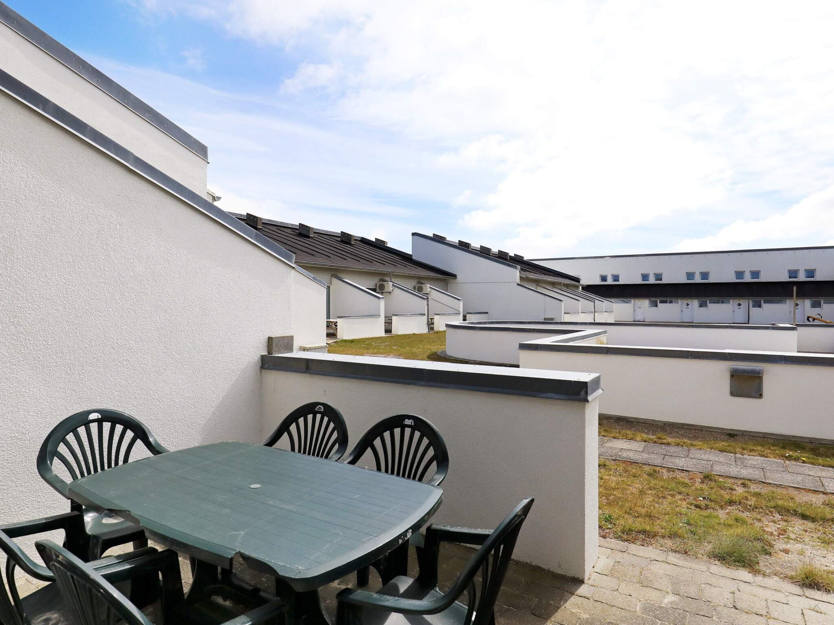 Une terrasse sur le toit, avec une table et des chaises, entourée de bâtiments blancs à toit plat.