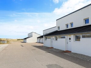 A row of white buildings with numbered doors, a gravel driveway, and a clear sky.