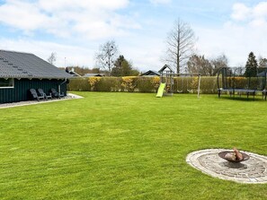 A well-maintained backyard with a green lawn, a wooden playhouse, and a swing set. - Holiday Home in Sydals (Sydals)