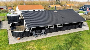 En moderne bygning med fladt tag, et overdækket udendørs loungeområde med stole og en lille træterrasse.