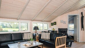 A modern living room with a black leather sofa, a wooden coffee table, and a black leather chair. There are large windows providing natural light and a view of the outdoors. - Holiday Home in Sydals (Sydals)