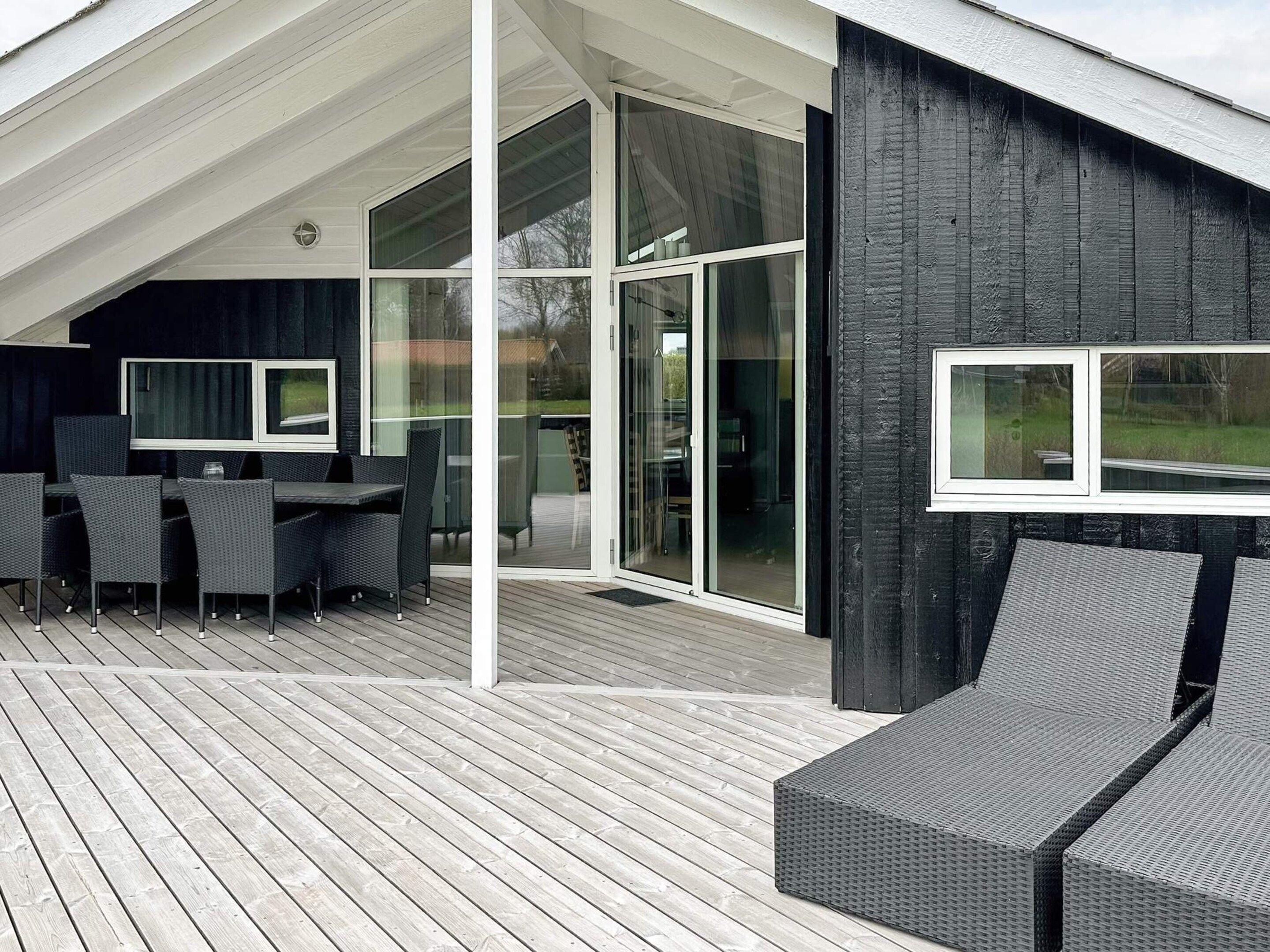 Une terrasse extérieure moderne dotée d’un espace repas, de grandes portes-fenêtres coulissantes et d’un mur en bois foncé.