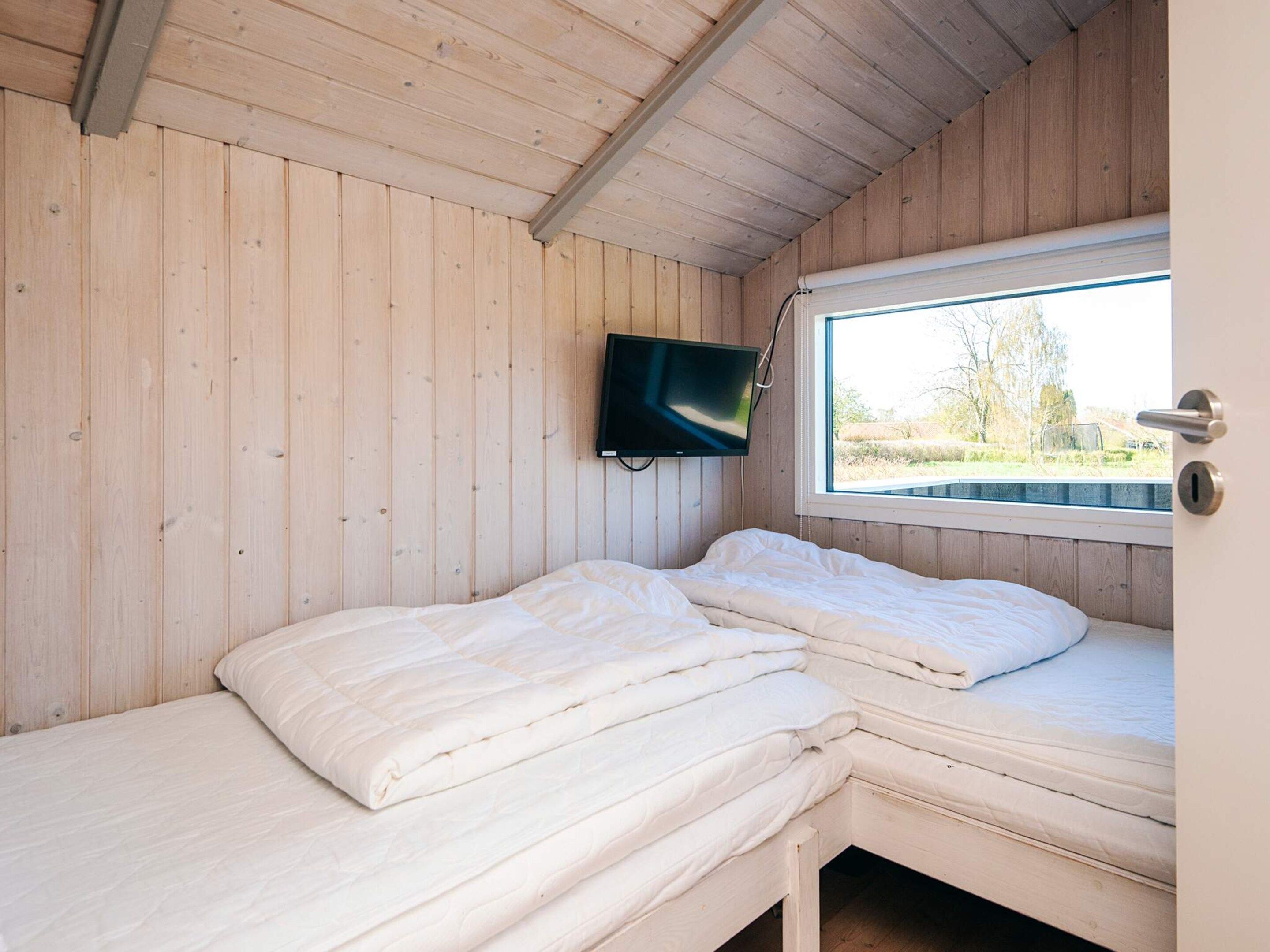 A cabin room with two beds, a television mounted on the wall, and a window with a view of the outdoors.