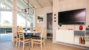 A modern interior with a dining area, a TV mounted on a wooden wall, and an air conditioning unit. - Holiday Home in Sydals (Sydals)