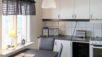 Een keuken met witte kasten, een zwart aanrecht, een raam met een zwart-wit geruit gordijn, een witte hanglamp, een broodrooster, een radio en een klok aan de muur.