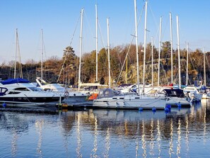 A marina with multiple sailboats docked, calm water, and a forested hillside in the background. - 4 Star Holiday Home in Stromstad (Stromstad)