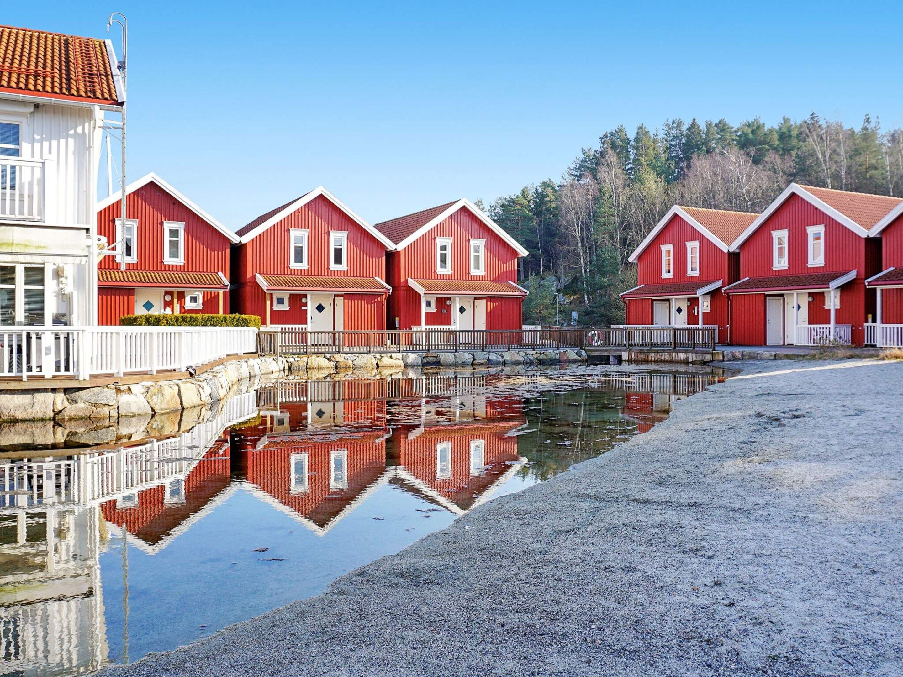 Filas de casas rojas de madera con detalles blancos, un muro de piedra y una masa de agua tranquila que refleja las construcciones.