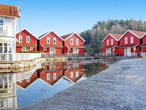 A row of red wooden houses with white trim, a stone wall, and a calm water body reflecting the buildings. - 4 Star Holiday Home in Stromstad (Stromstad)