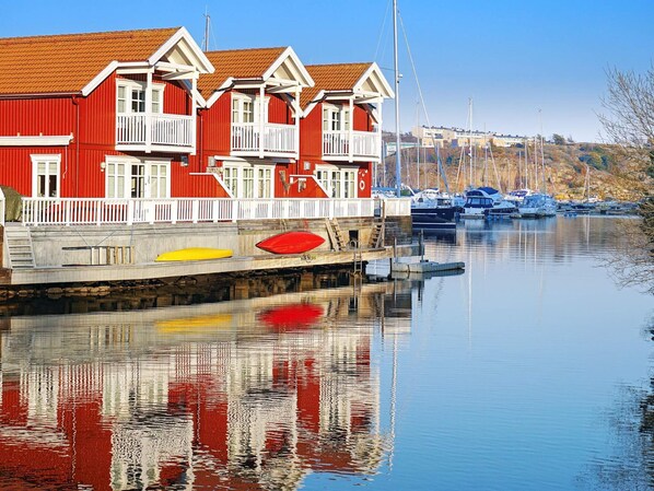 A waterfront building with a red facade and white trim, reflecting in calm water.