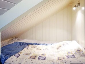 A room with a sloped ceiling, a bed with a patterned bedspread, and a wall-mounted light fixture. - 4 Star Holiday Home in Stromstad (Stromstad)
