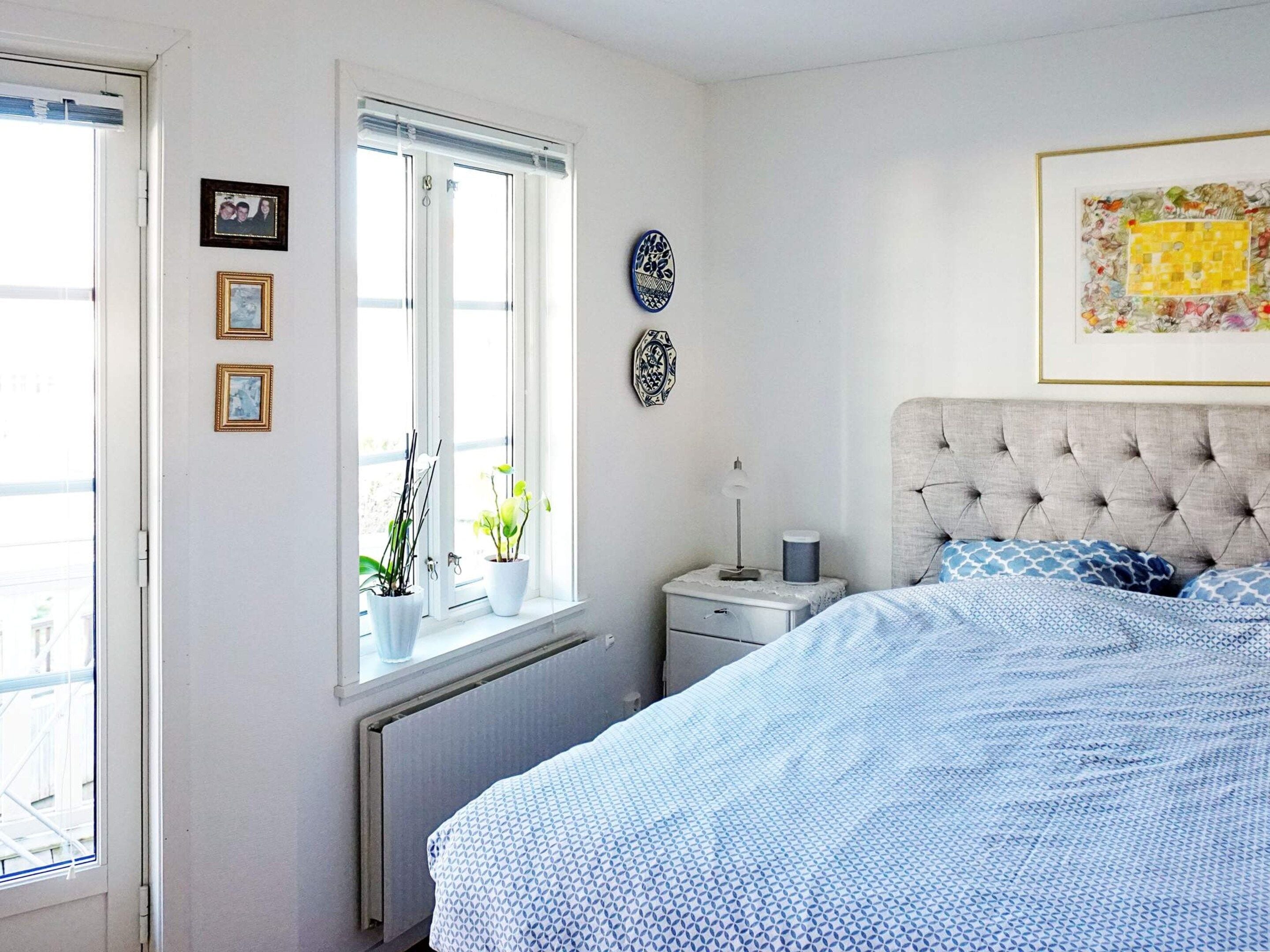 Un dormitorio con cama, mesita de noche, ventana con plantas y adornos en la pared.