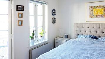 Un dormitorio con cama, mesita de noche, ventana con plantas y adornos en la pared.