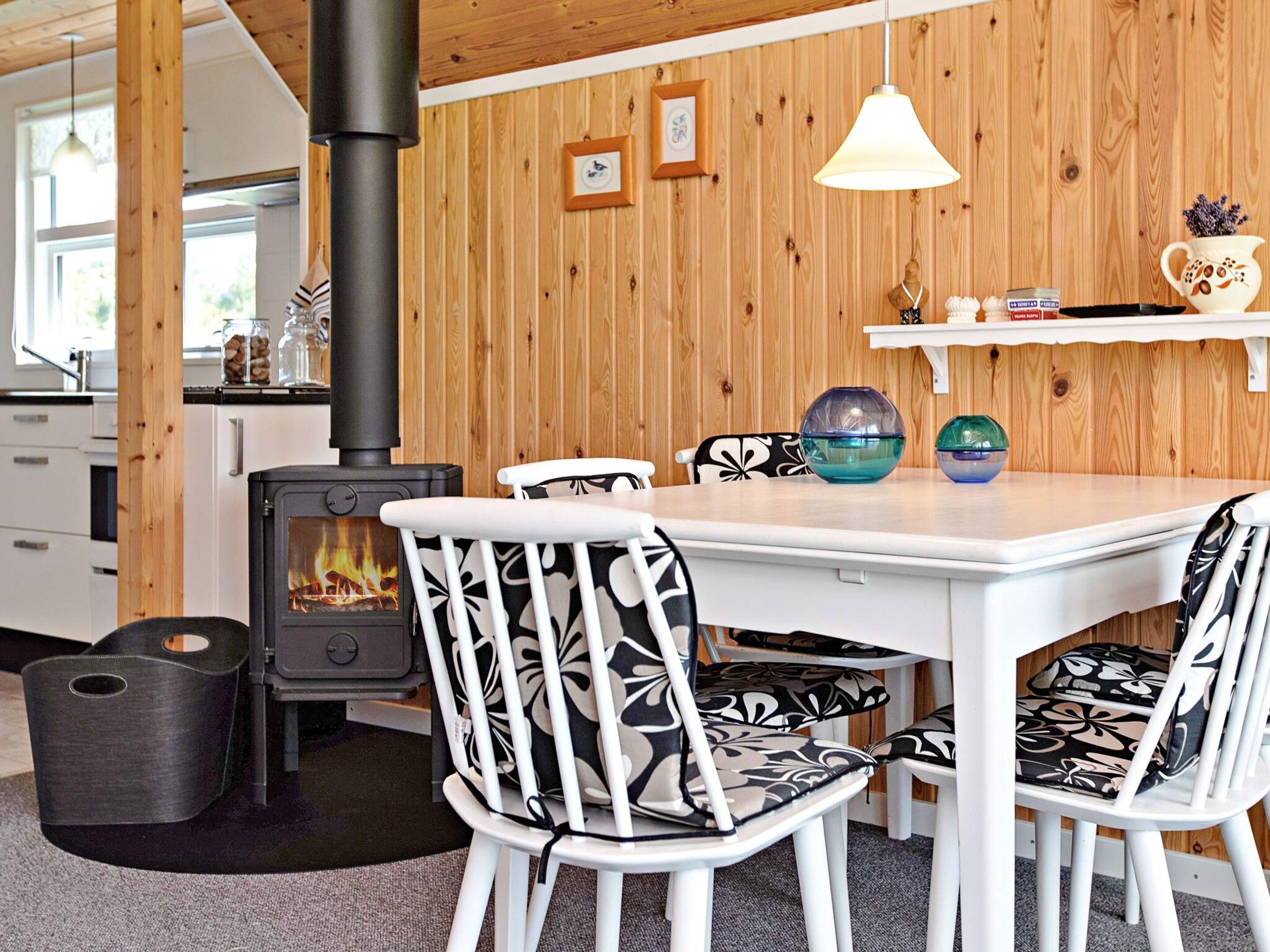 Et hyggeligt rum med brændeovn, hvidt møblement og en trævæg.