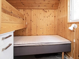 Una habitación pequeña con cama individual, techo y paredes de madera, una lámpara de noche y una ventana.