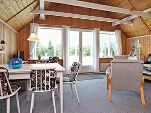 A cozy room with a wooden ceiling, a dining table with chairs, a sofa, and a large window with curtains.