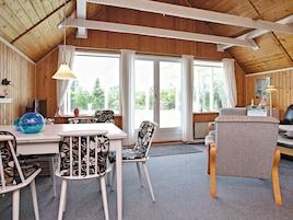 A cozy room with a wooden ceiling, a dining table with chairs, a sofa, and a large window with curtains.