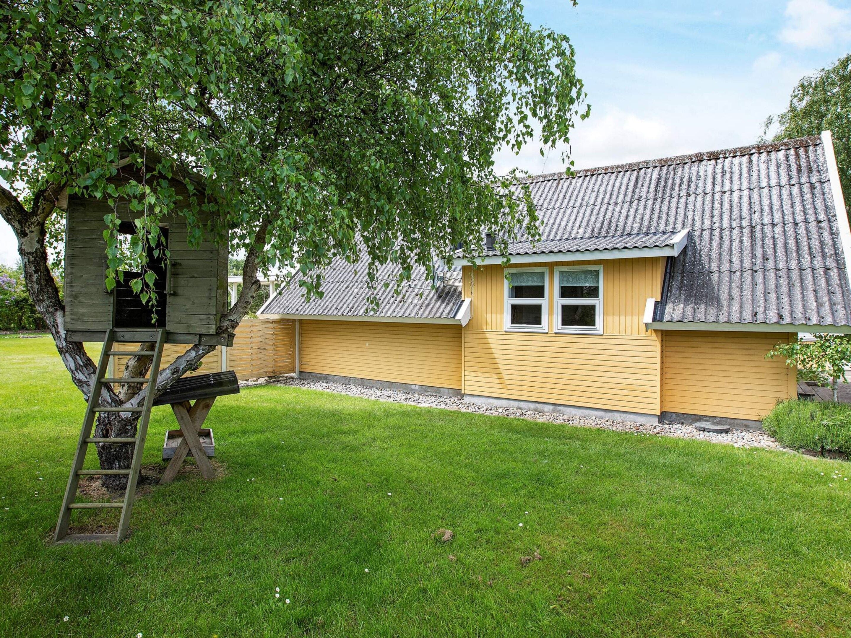 A yellow building with a tiled roof, a wooden ladder, and a tree in the foreground.