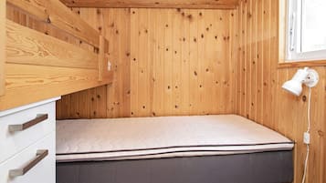 A small wooden room with a single bed, a white dresser with drawers, and a window with a white lamp.