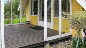 A covered porch with a wooden deck, large windows, and a small garden area with plants and a tree. - 4 Star Holiday Home in Dannemare (Dannemare)