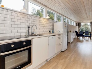 A modern kitchen with white cabinetry, a Bosch oven, and a dishwasher. There are two chairs and a table in the adjacent dining area. - Holiday Home in VÃ¦ggerlÃ¸se (Vaeggerlose)