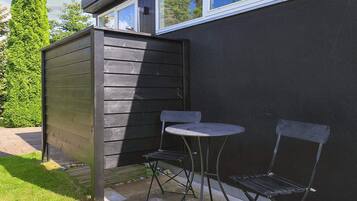 A small outdoor seating area with a table and two chairs, adjacent to a building with a dark exterior and windows.