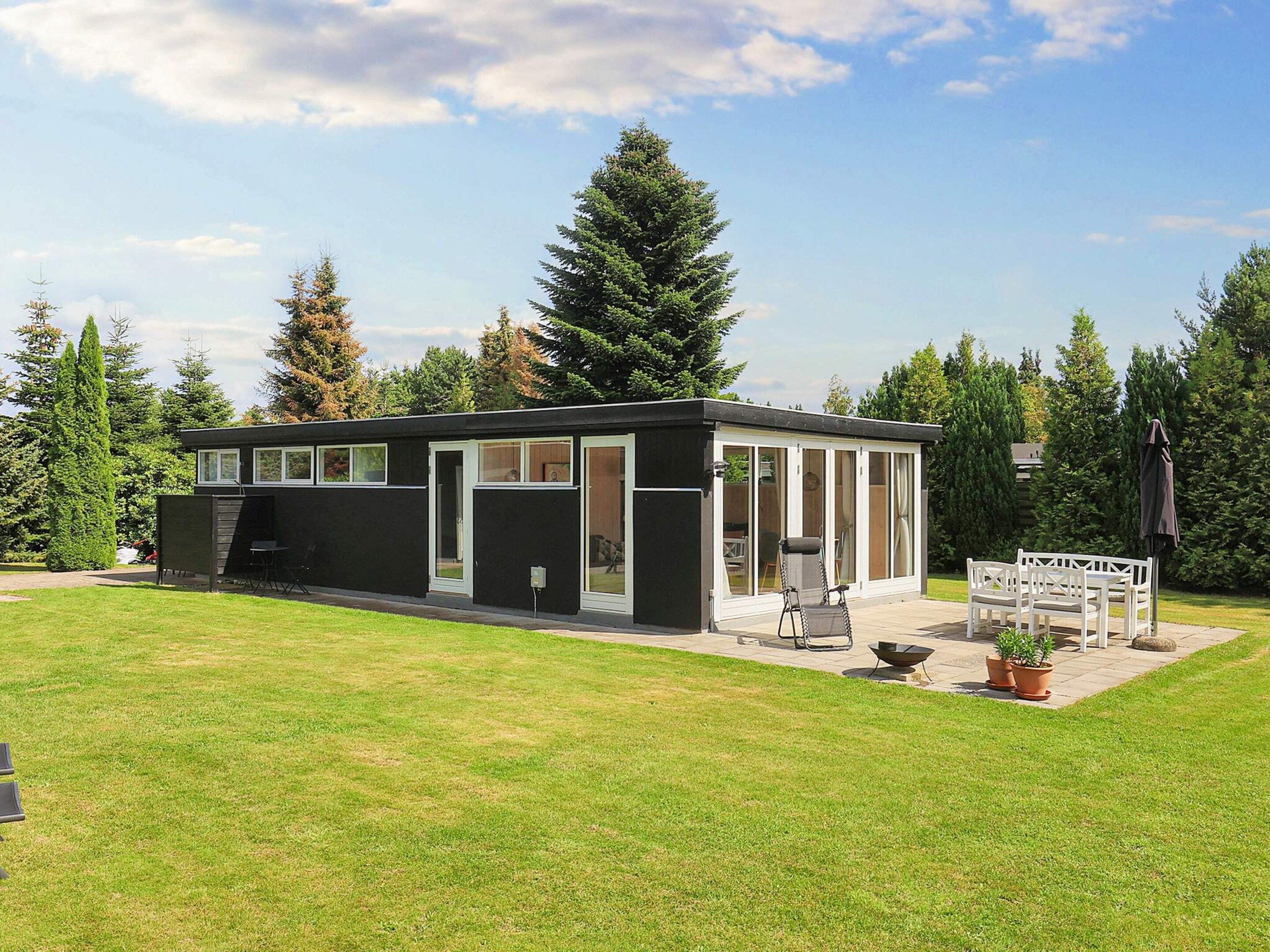 A modern, single-story building with a covered patio area, surrounded by a well-maintained lawn and tall trees.