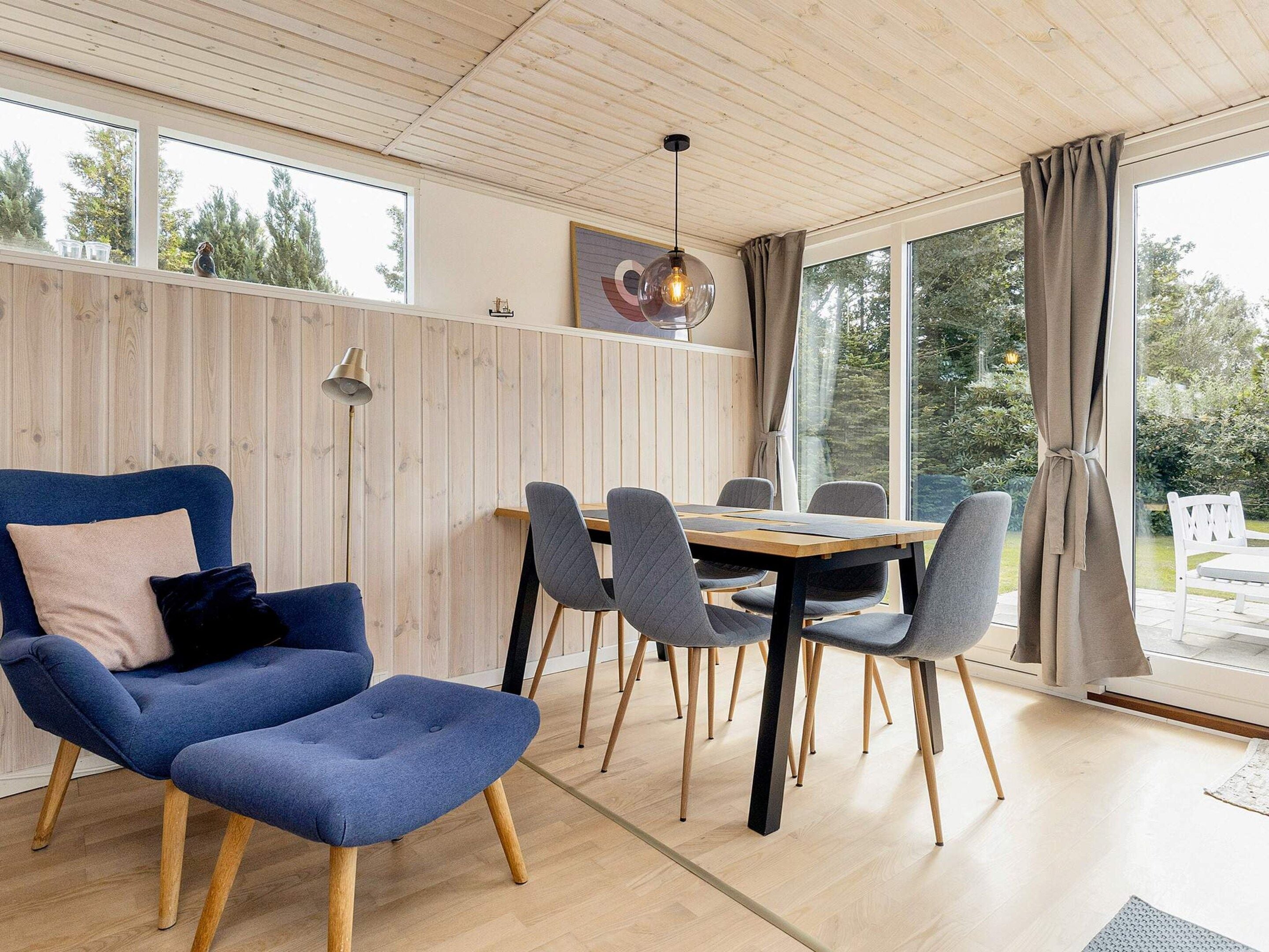 A modern interior with a wooden ceiling, a dining table with chairs, and a large window with curtains.