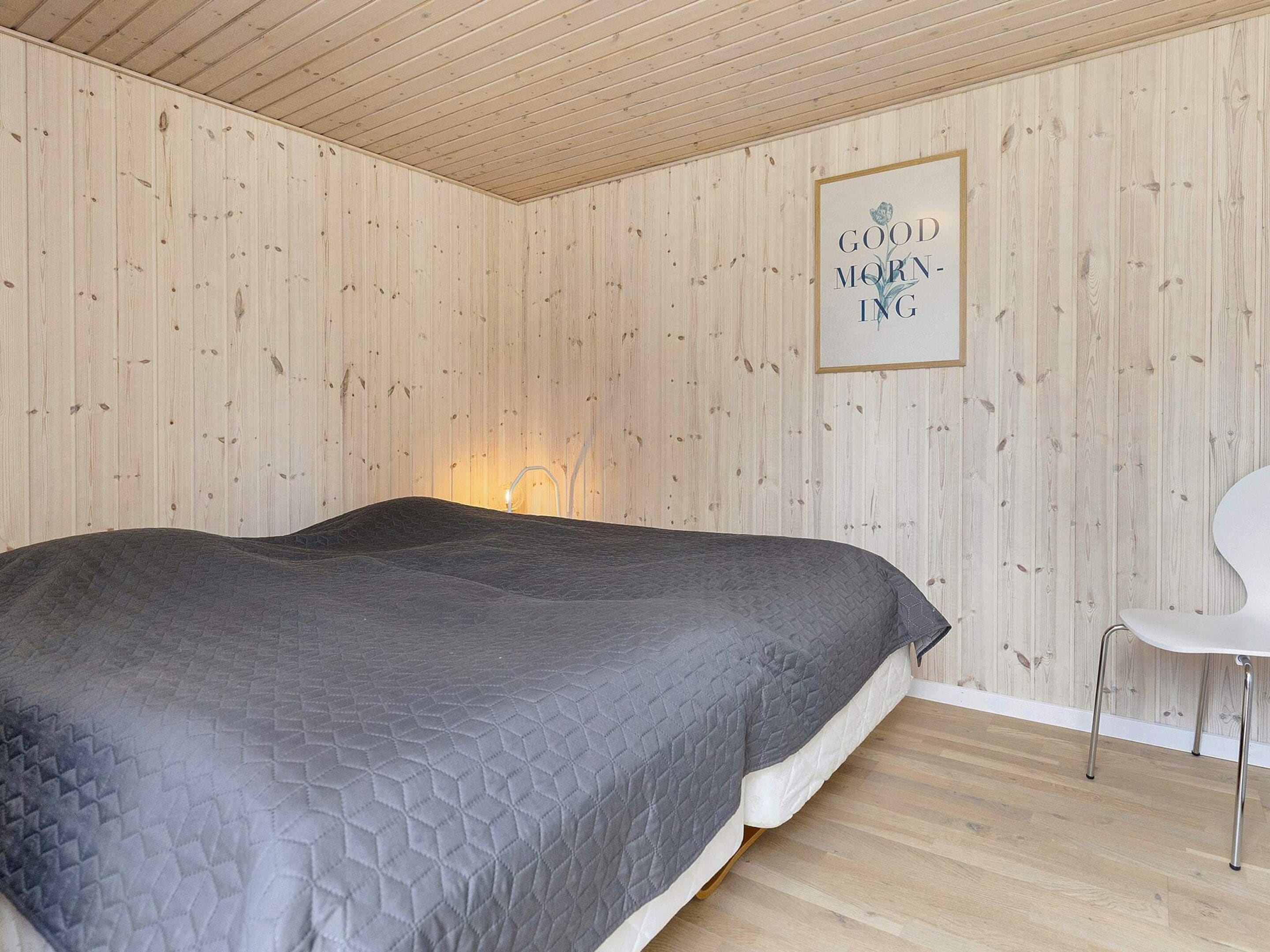 A bedroom with a bed, a chair, and a wall-mounted picture frame with text.