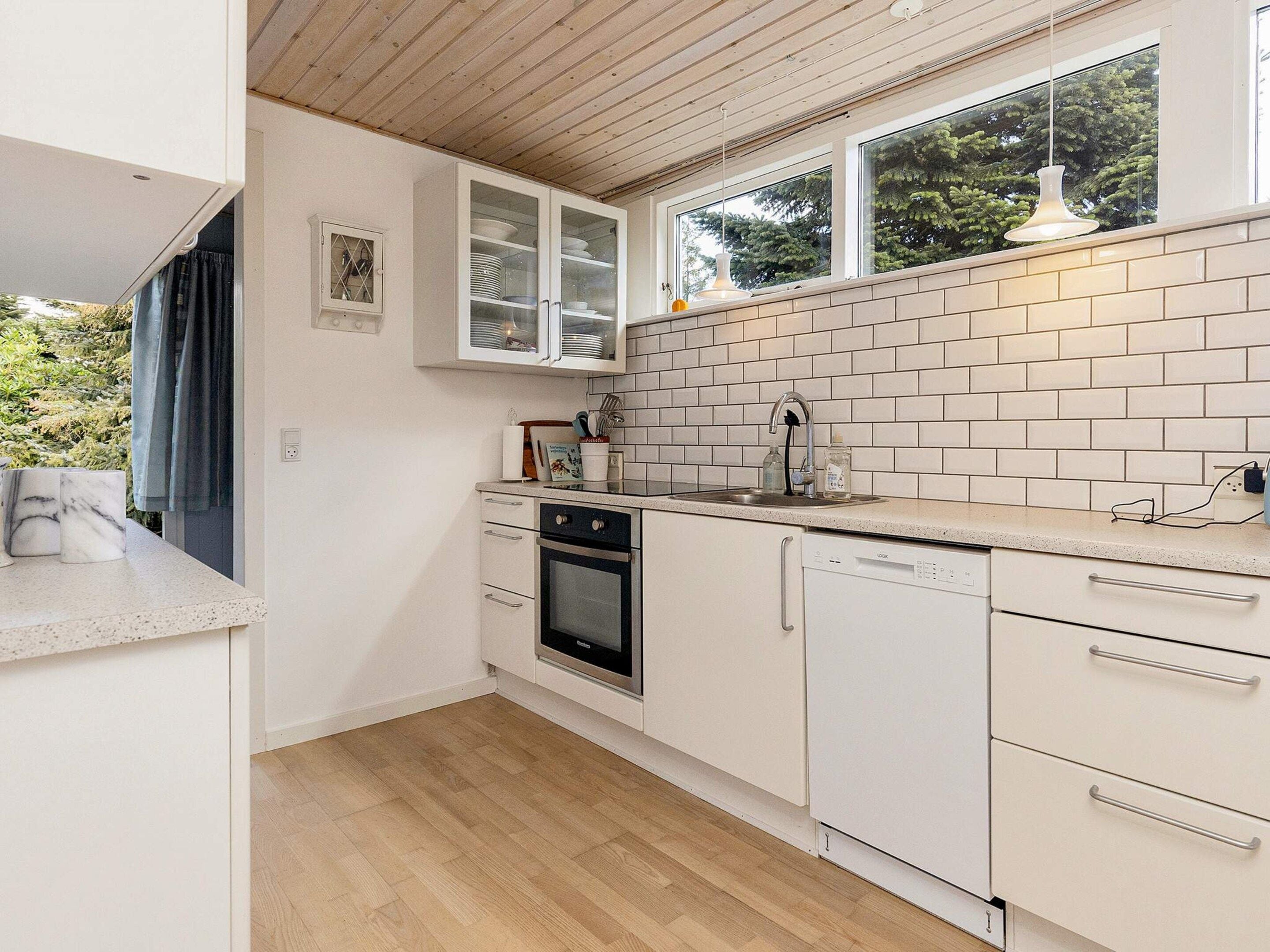 A modern kitchen with white cabinetry, a built-in oven, a dishwasher, and a window above the sink.