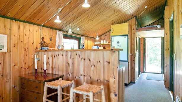 A wooden interior with a kitchen area, wooden stools, and a refrigerator.